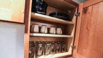 A wooden cabinet with shelves containing glass jars, ceramic mugs, and black plates.
