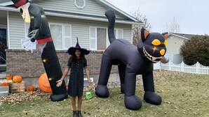 A person in a witch costume standing in front of a house with Halloween decorations. - Kingston East (Rexburg)