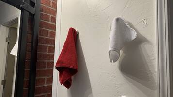 Un bagno con un asciugamano rosso appeso a un porta asciugamani, un asciugamano bianco su un scaldasalviette a parete, uno specchio e un muro in mattoni.