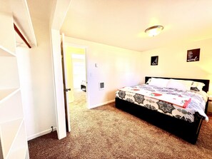 A bedroom with a bed, a door leading to another room, and a ceiling light. - Kingston East (Rexburg)