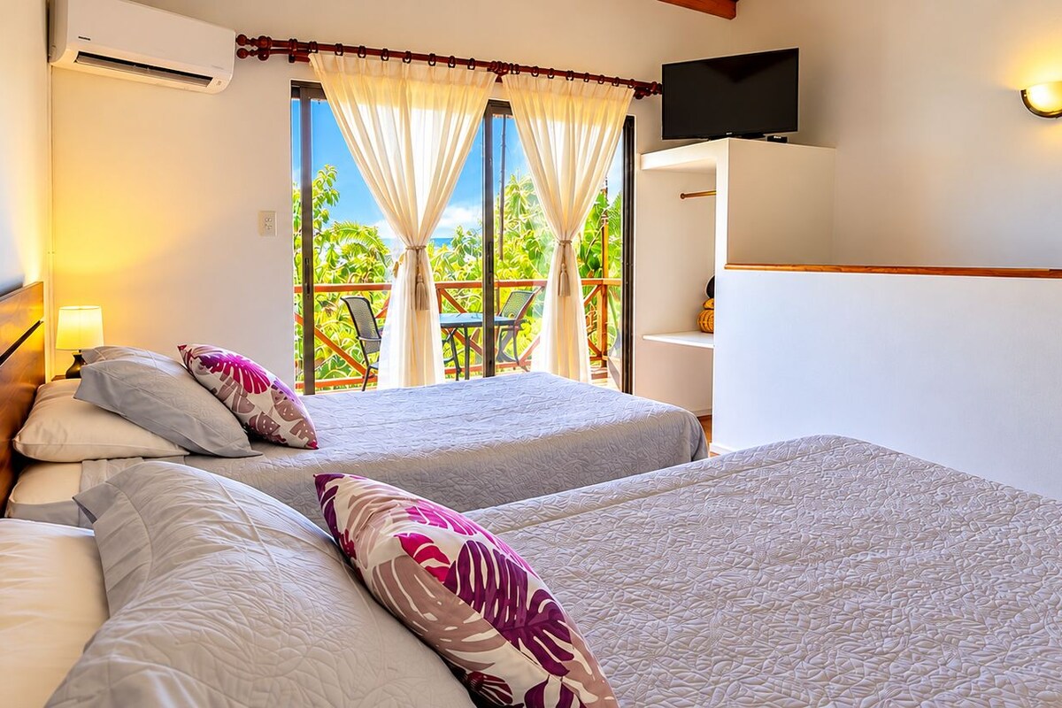 Une chambre d’hôtel avec deux lits, une télévision et un balcon donnant sur des palmiers.