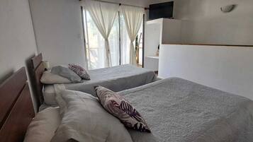 Hotellihuone, jossa on kaksi sänkyä, seinälle asennettu televisio ja ikkuna, jossa on verhot.