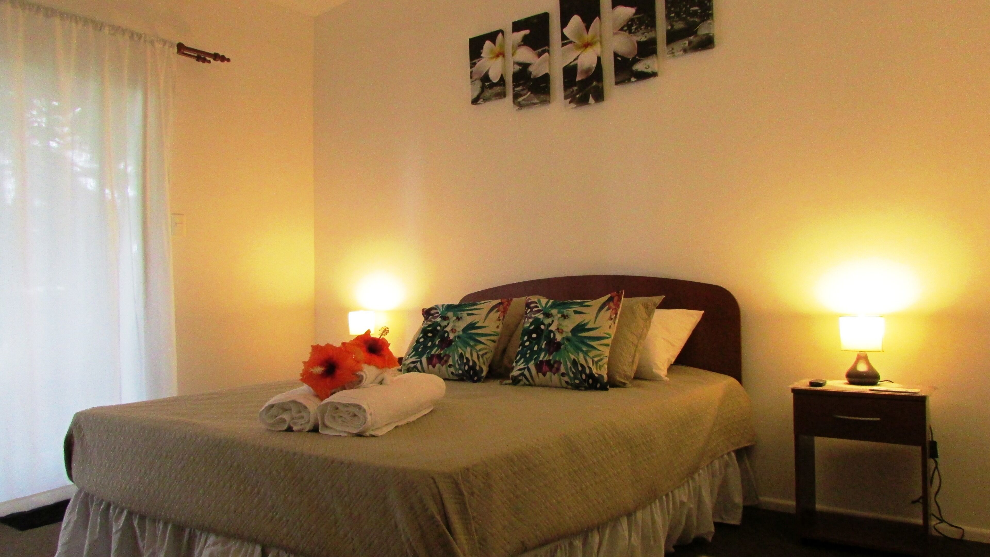 A neatly made bed with a floral pillow, a rolled towel, and a small table with a lamp beside it.
