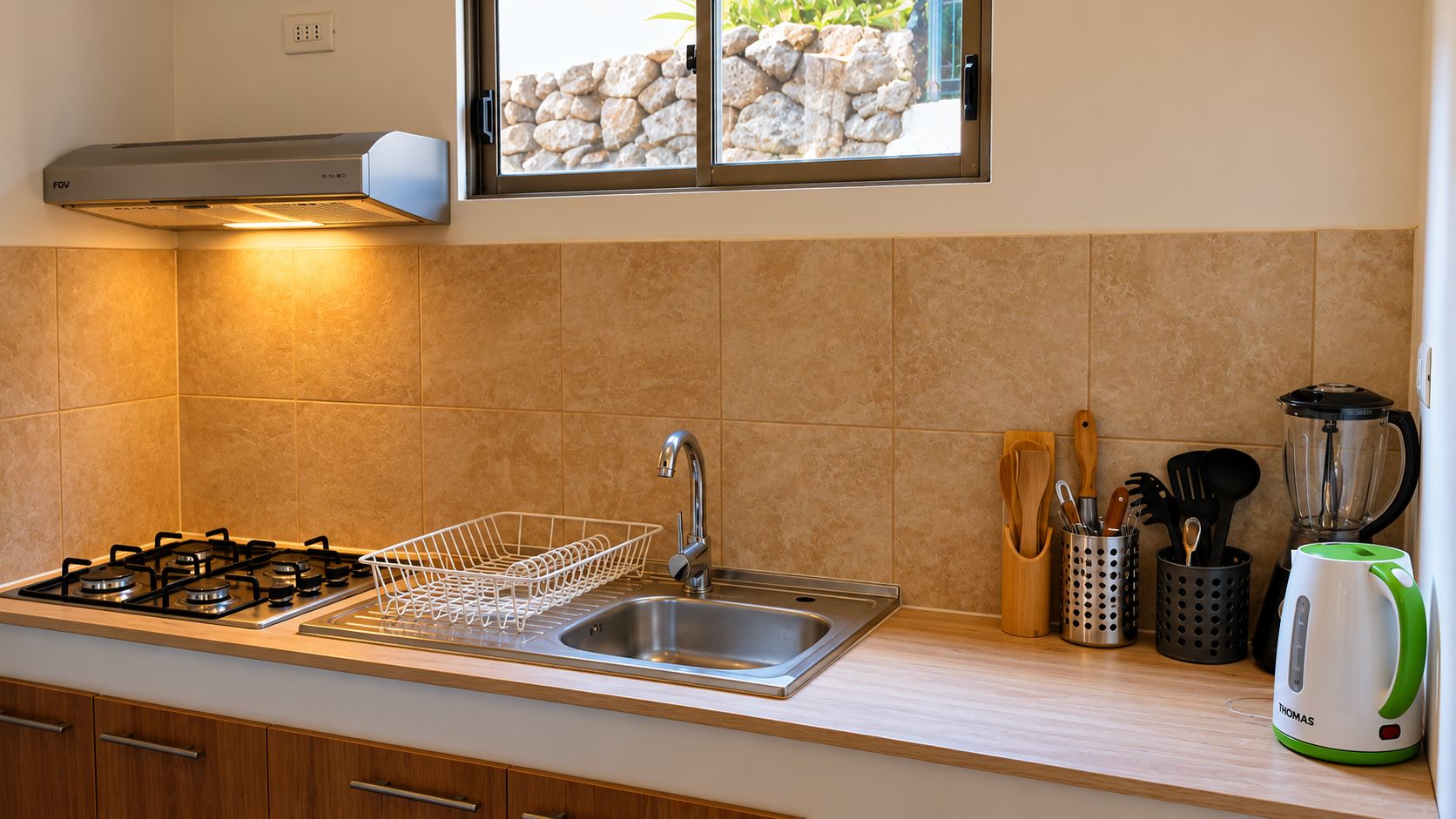 Une cuisine moderne équipée d’une cuisinière à gaz, d’un évier en acier inoxydable et d’une fenêtre donnant sur un mur en pierre.