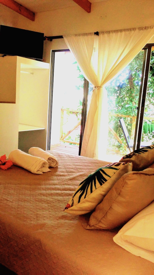 A bed with a canopy, a window with curtains, and a view of greenery outside.