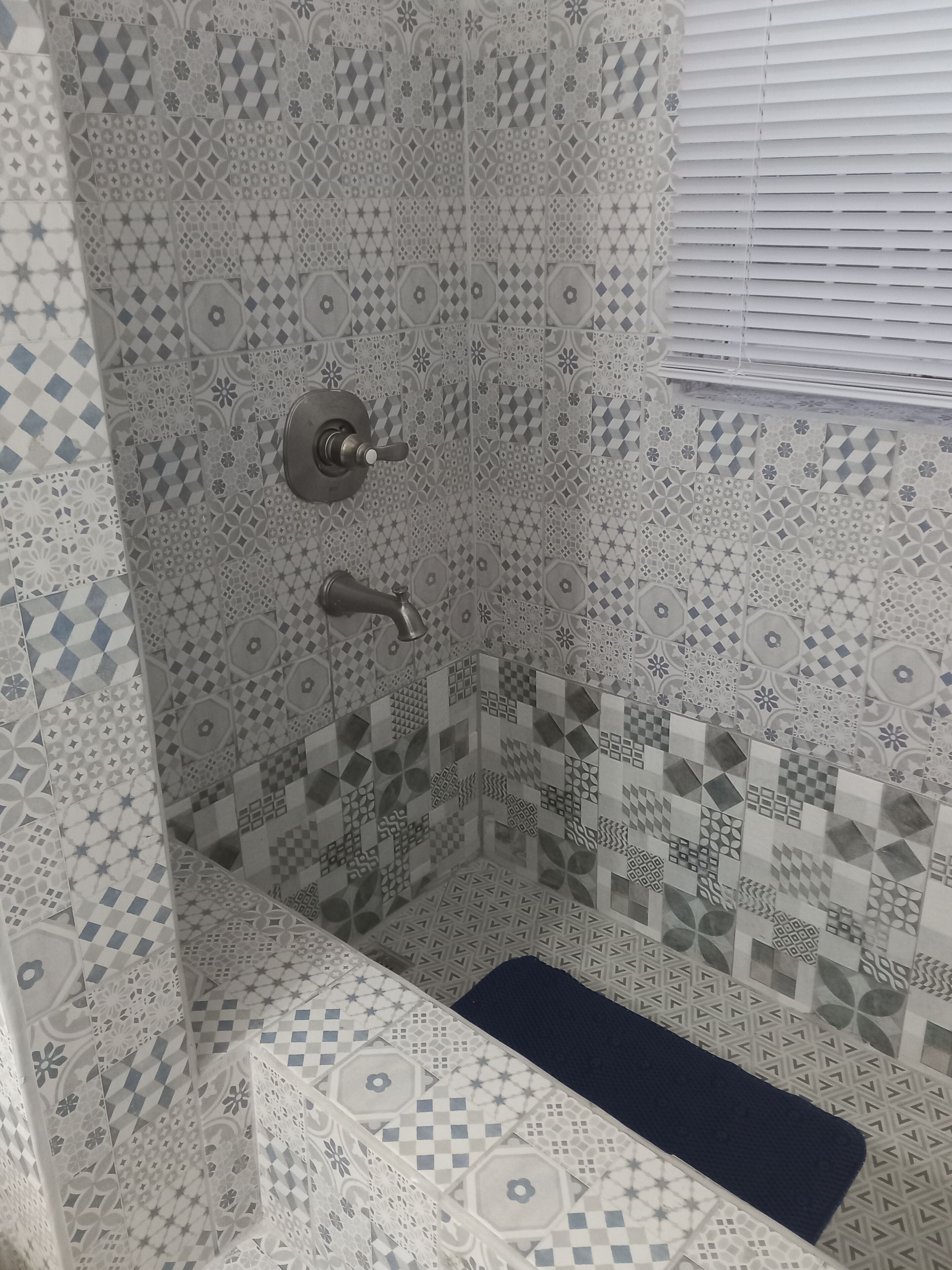 A shower with a geometric tile pattern and a blue bath mat.