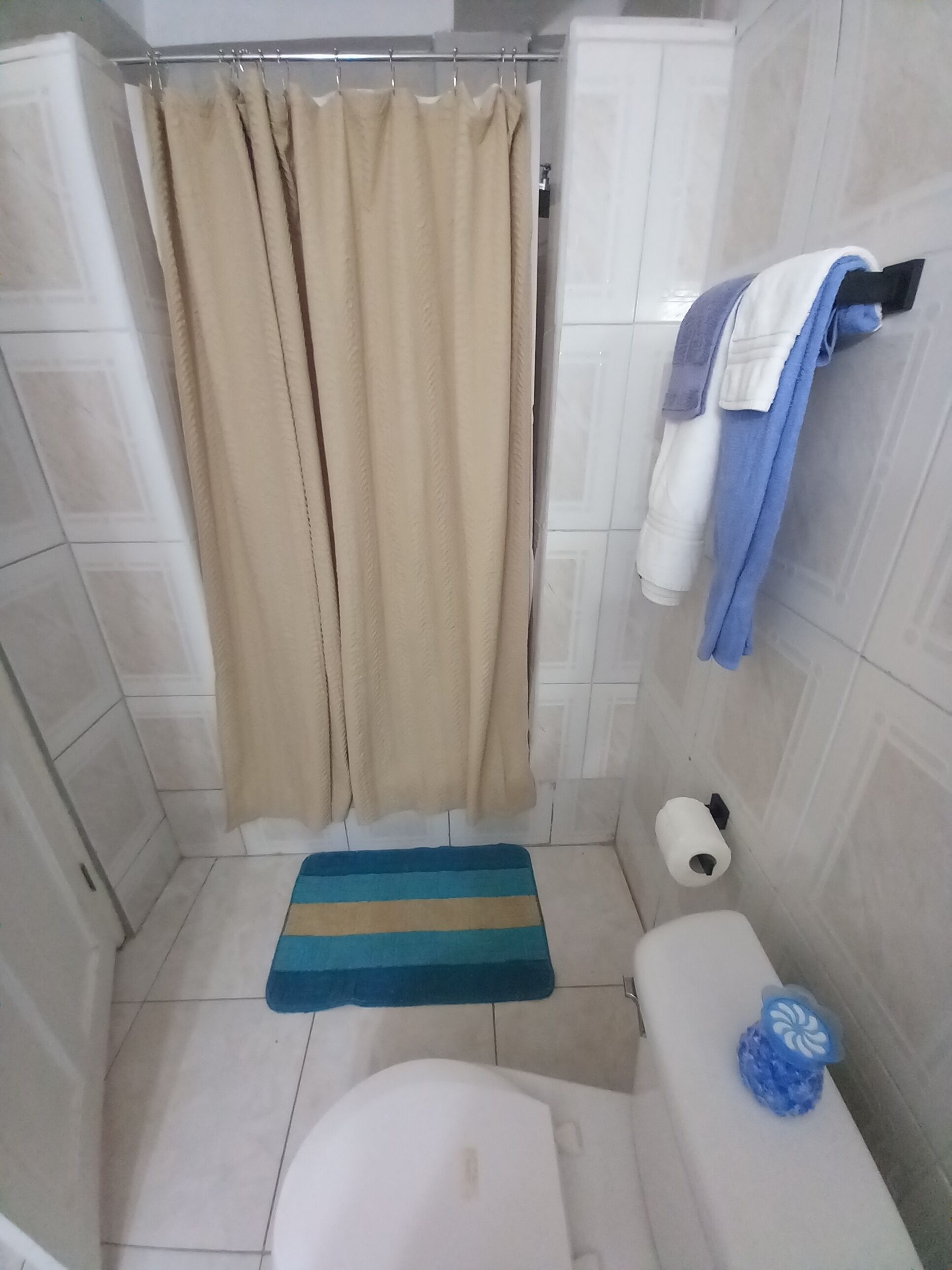 A small bathroom with a shower curtain, a toilet, a towel rack with towels, and a toilet paper holder.