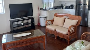 Een ruime woonkamer met een televisie, rieten meubels en een keuken op de achtergrond.