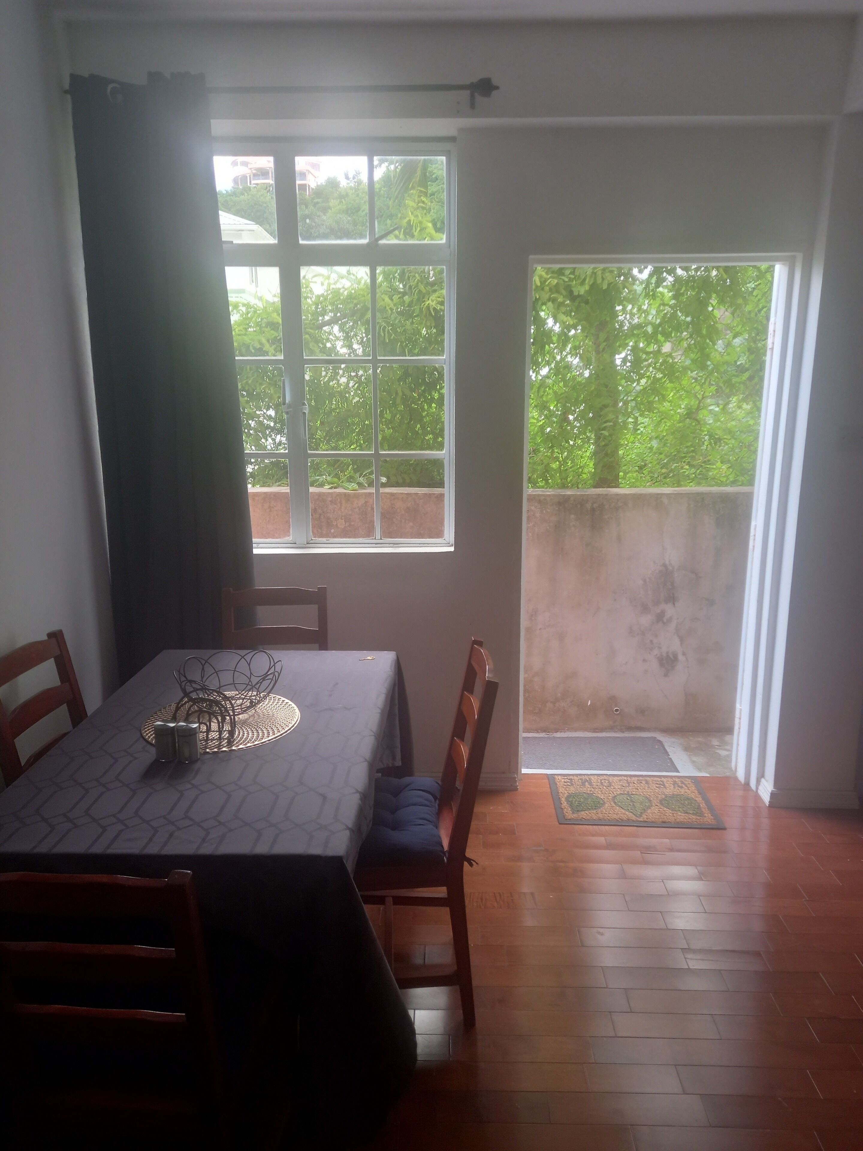 A dining area with a table set for two, a window with a view of greenery, and a door leading to an outdoor area.