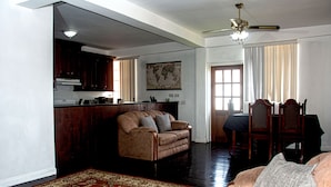 Een ruime woonkamer met een bank, een salontafel en een eettafel met stoelen. Er is een keuken met donkere houten kastjes en een wereldkaart aan de muur.