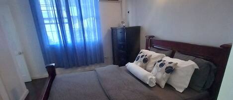 A bedroom with a bed, a dresser, a nightstand, and a wall-mounted lamp.