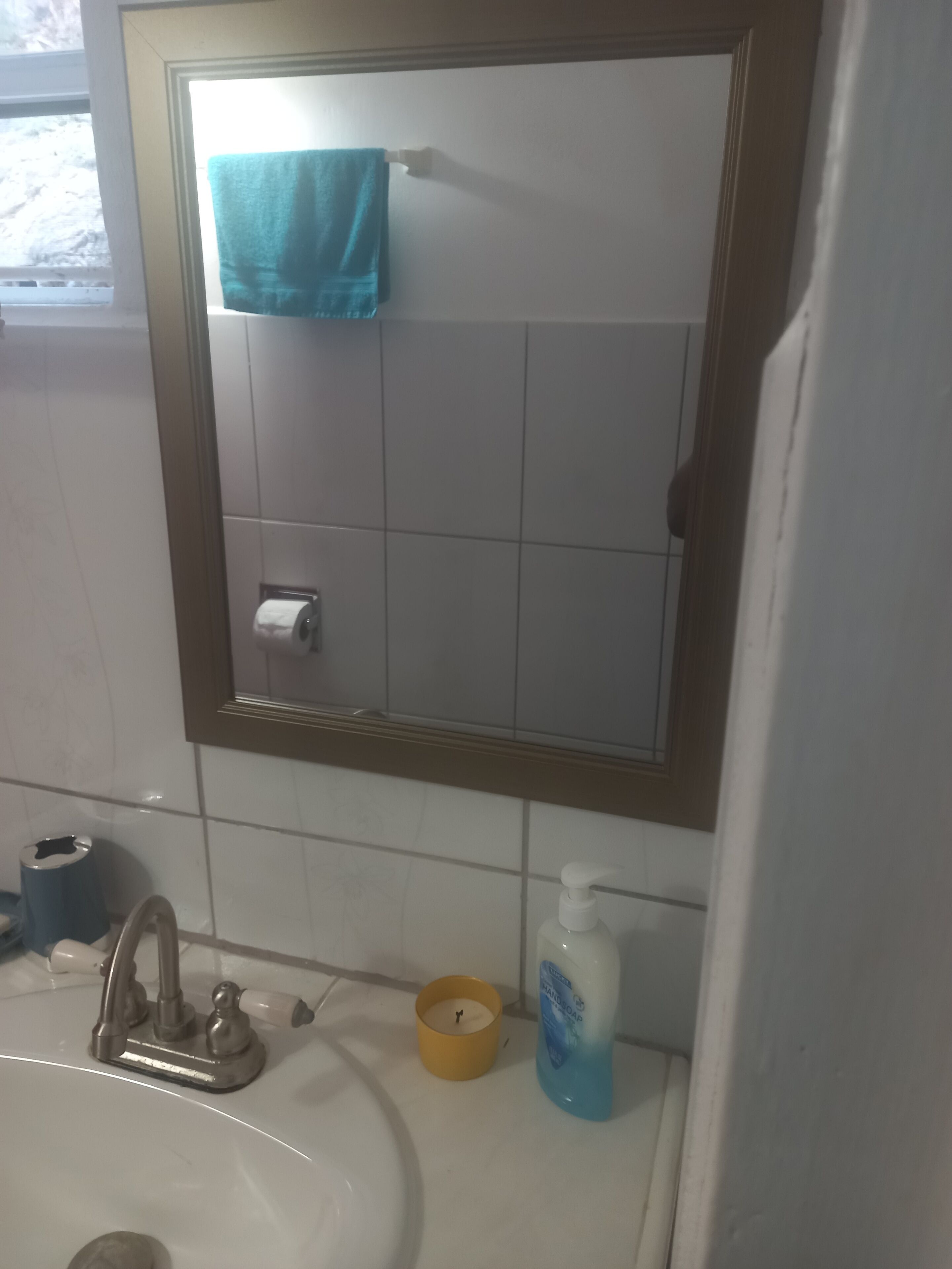 A bathroom with a sink, a mirror, a towel, a candle, and a soap dispenser.