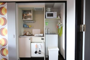 Una kitchenette compacta equipada con refrigerador, microondas y lavamanos pequeño.