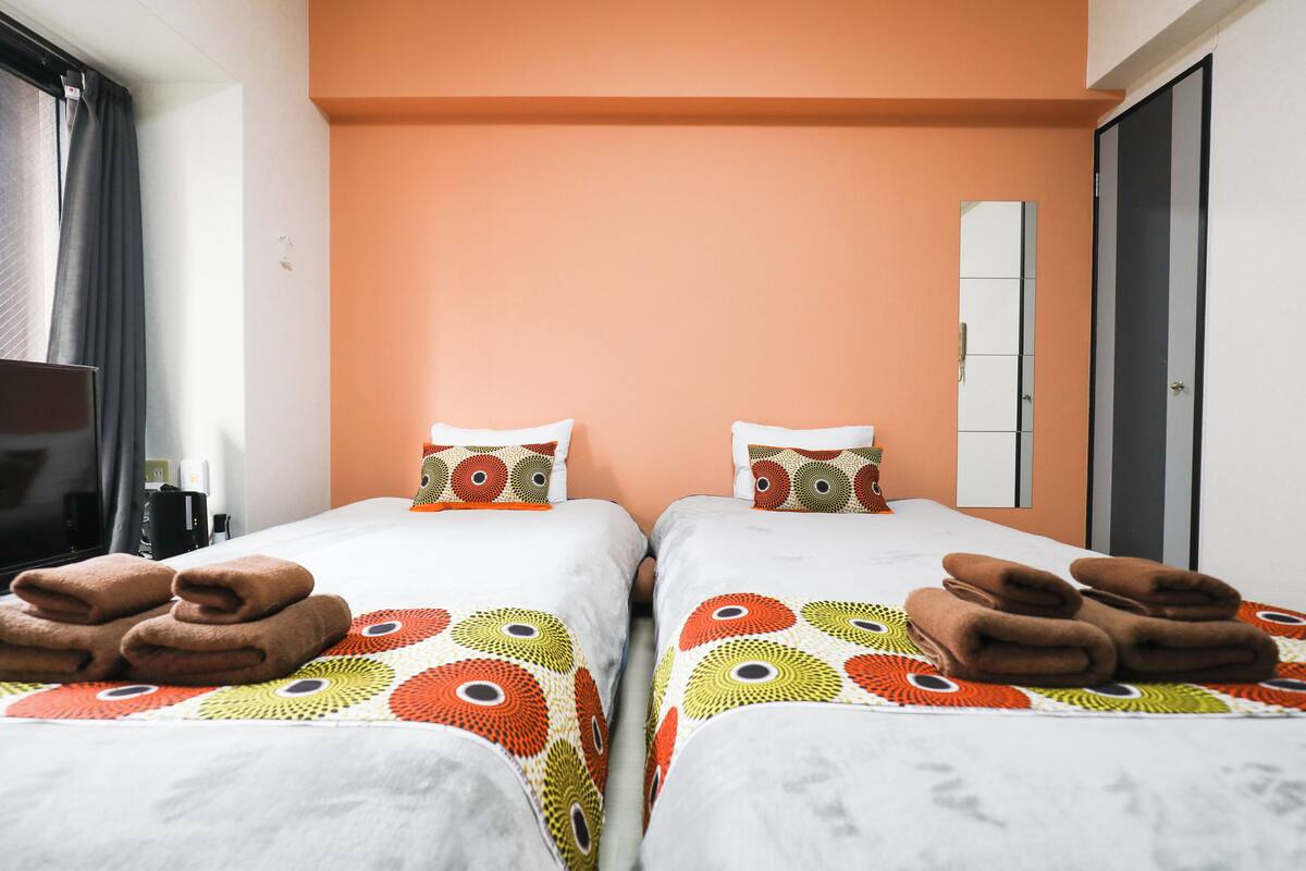 A hotel room with two beds, each with a patterned bedspread and pillows, and towels neatly folded on the beds.