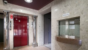 Um saguão de hotel com um elevador vermelho, uma mesa de recepção e um aviso indicando área exclusiva para funcionários.