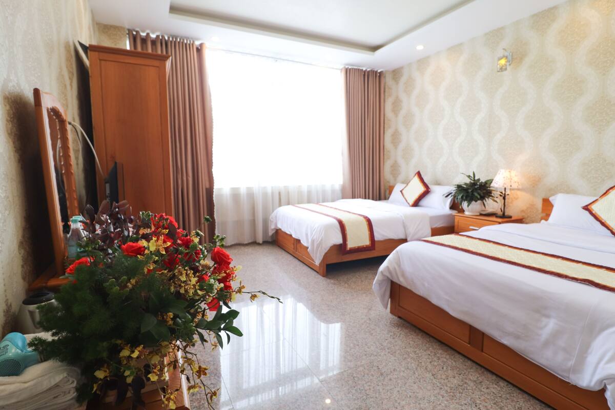 Habitación de hotel con dos camas, un espejo grande, una planta en maceta y una ventana con cortinas.
