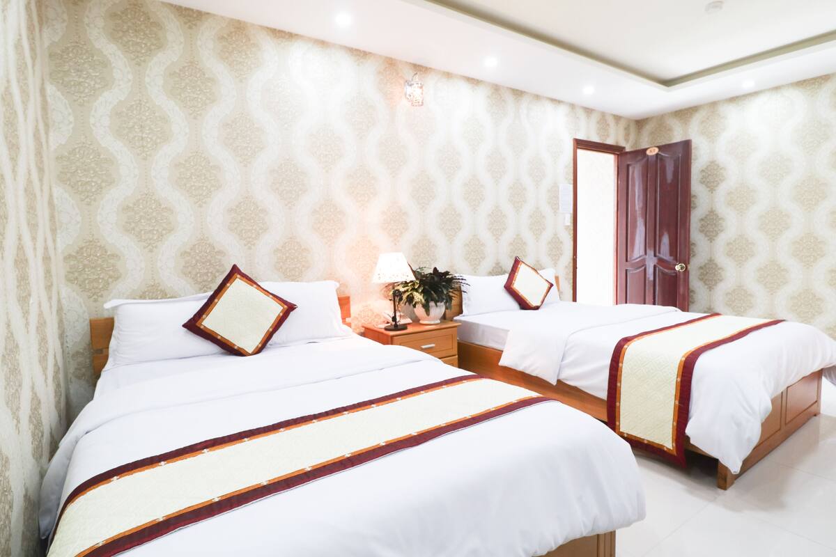 Una habitación de hotel con dos camas, una mesita de noche con lámpara y una puerta.