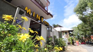 Hotel 'MINE HOTEL' con un letrero, rodeado de follaje y un cielo despejado.