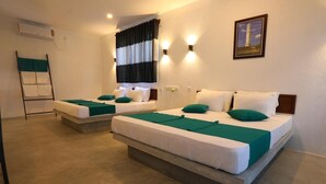 Camera d'albergo con due letti singoli, ognuno con copriletto verde e cuscini bianchi. Si vede una finestra con tende bianche e nere, un condizionatore d'aria a parete e un quadro appeso raffigurante un faro.
