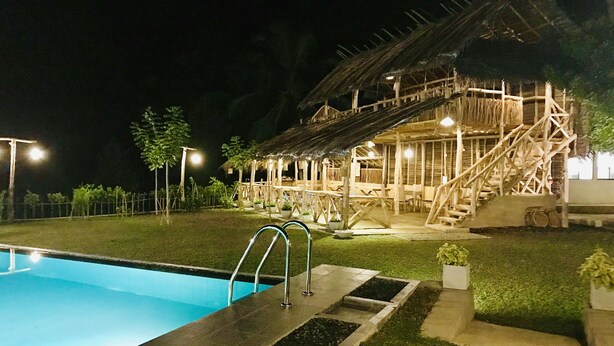 Una piscina con bordo in legno, una struttura con tetto di paglia e una scala che conduce a una zona coperta.