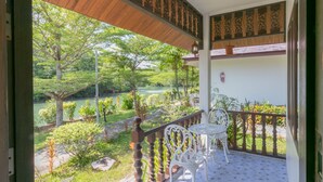 Un balcon donnant sur un jardin et un plan d’eau. On y trouve deux chaises blanches et une petite table.