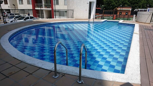 A swimming pool with a checkered pattern, metal ladders, and a tiled deck. - Apartamento Prados Del Norte (Cali)