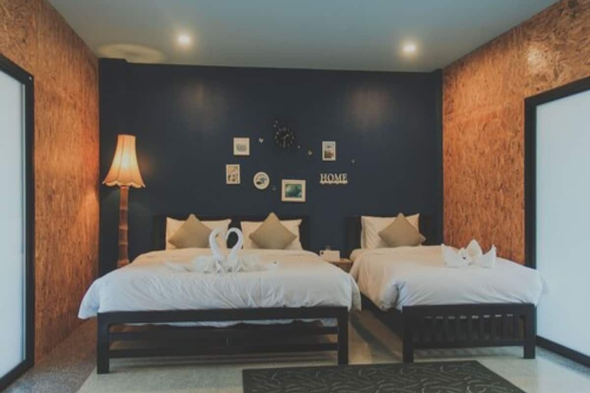 A hotel room with two beds, a lamp, wall art, and a 'HOME' sign.