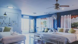 Habitación de hotel con dos camas, ventilador de techo, un ventanal grande y un mural en la pared.