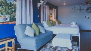 Una habitación con una pared azul de acento, un sofá, una cama, una mesita y un ventilador de techo.