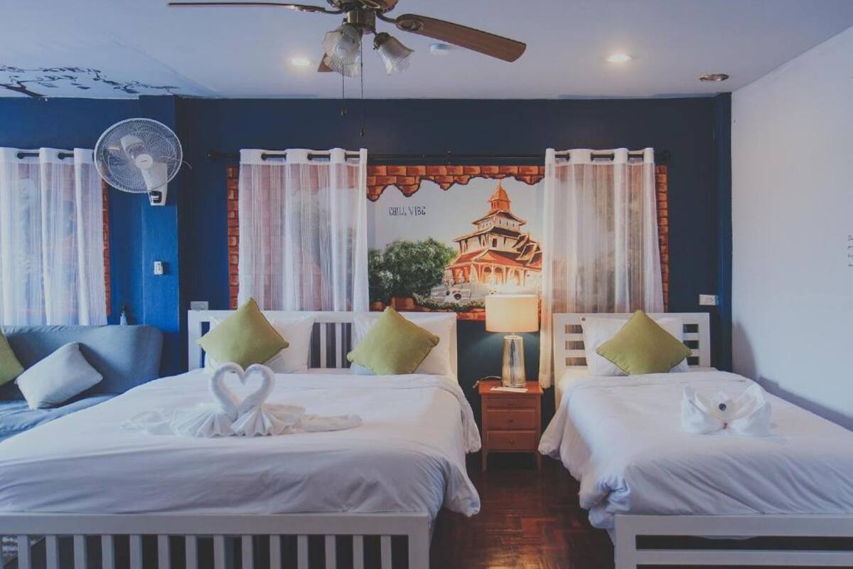 A hotel room with two beds, a ceiling fan, a wall mural, and a nightstand with a lamp.