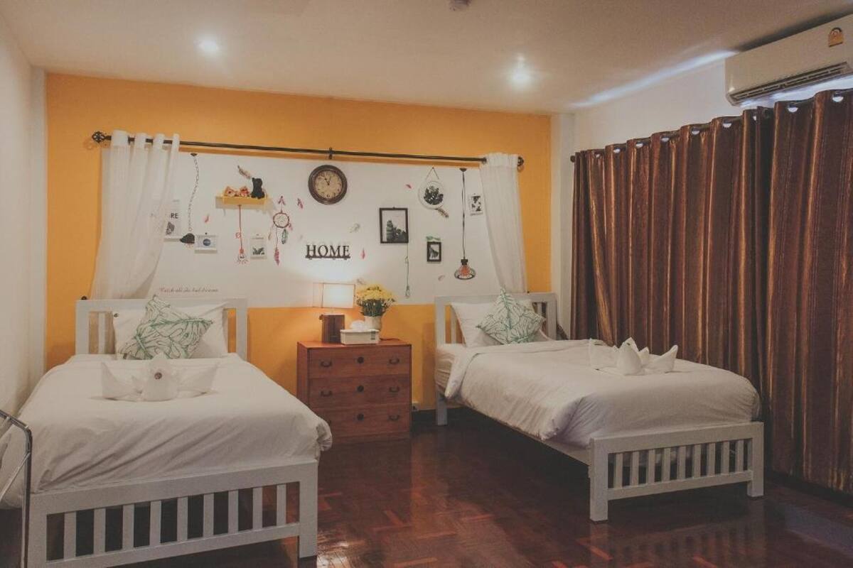 A bedroom with two beds, a dresser, a clock, and a wall with various decorations.