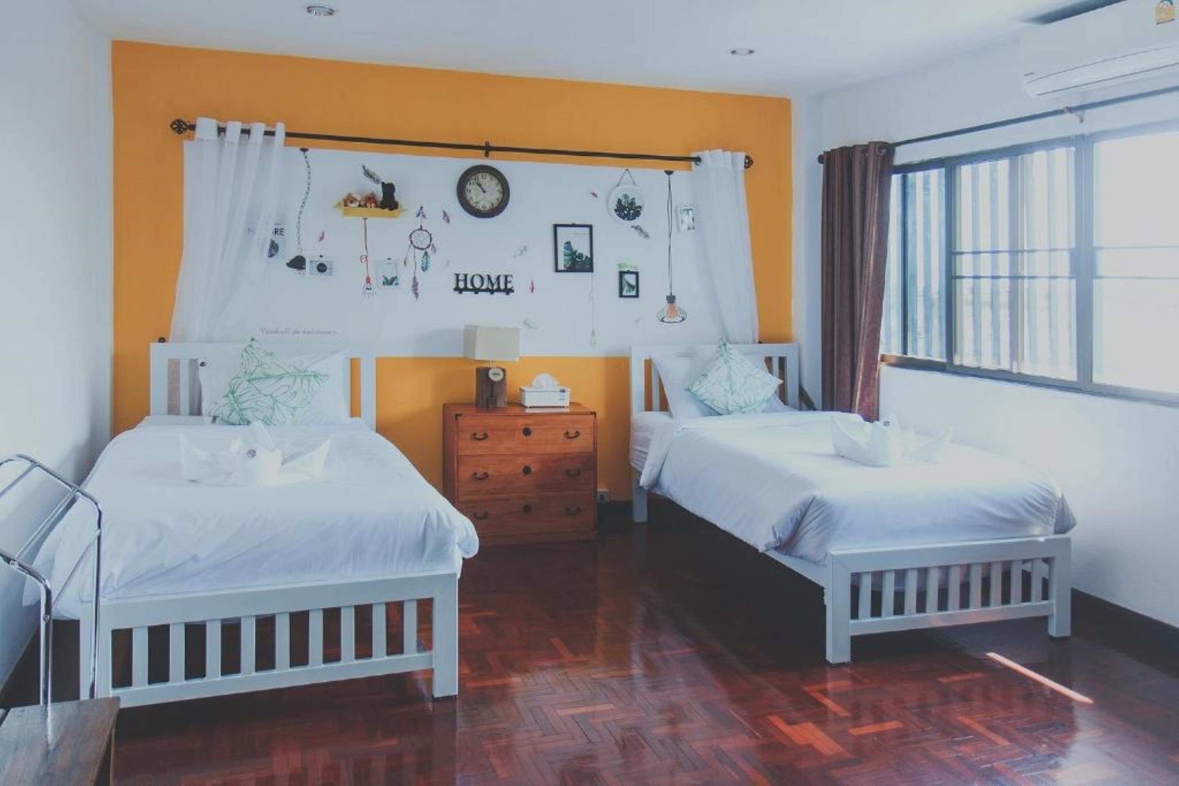 A bedroom with two beds, a wooden dresser, a wall clock, and a window with curtains.