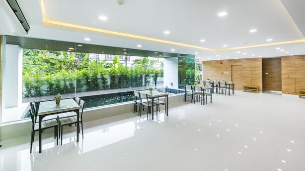 A modern hotel lobby with a glass wall, indoor plants, and a pool view. - Thawan Apartment (Satun)