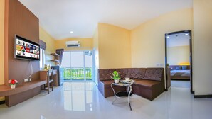 A modern hotel lobby with a flat-screen TV displaying news channels, a brown leather sofa, a small round table with a potted plant, and a glass door leading to a balcony. - Thawan Apartment (Satun)