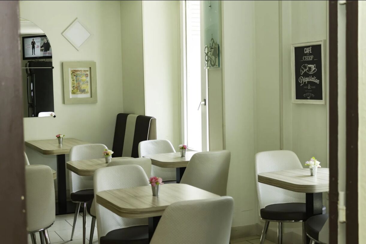 Zona pranzo con tavoli e sedie, un frigorifero, una televisione e una porta con un pannello di vetro.