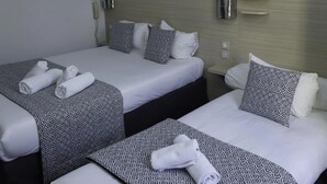 Ett hotellrum med två sängar, där varje säng har mönstrat sänglinne och kuddar, ett sängbord och en telefon som är monterad på väggen.