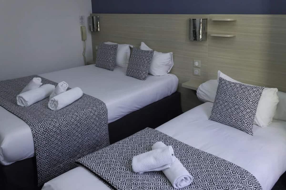 Habitación de hotel con dos camas, cada una con ropa de cama y almohadas estampadas, una mesita de noche y un teléfono en la pared.