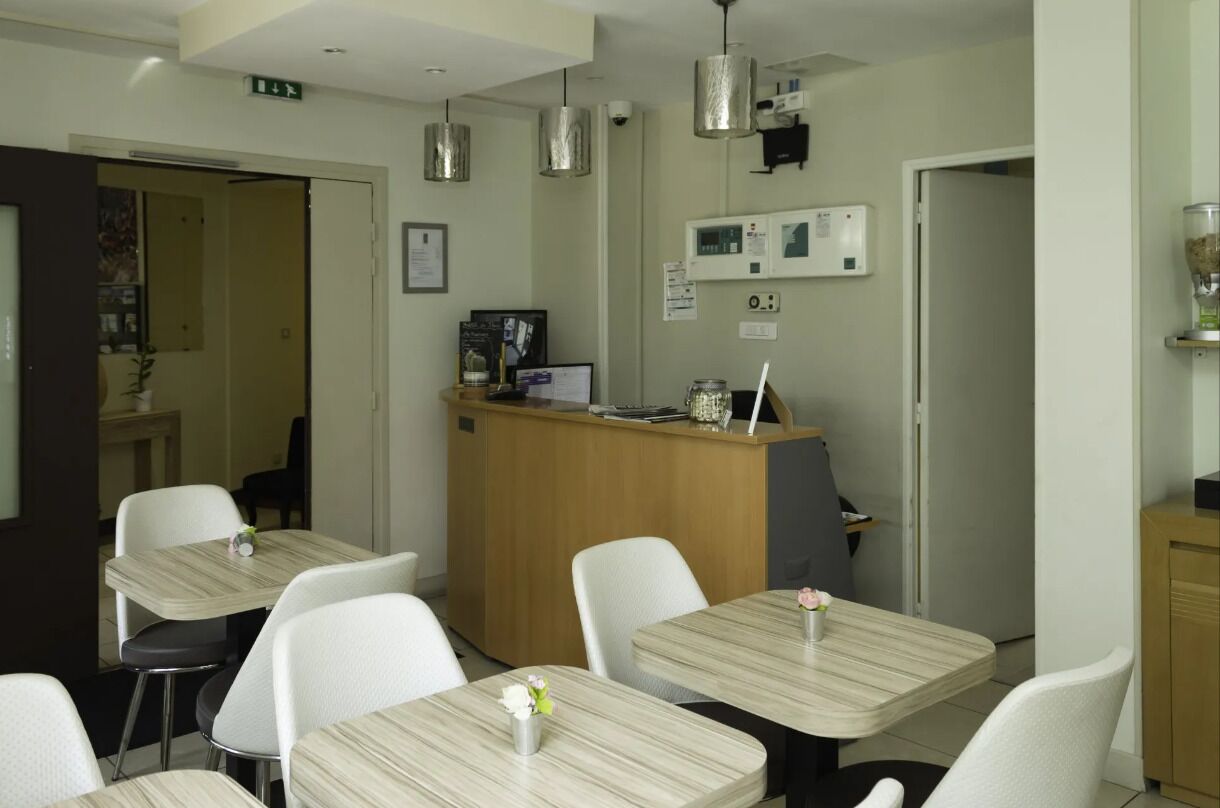 Une chambre d’hôtel avec un comptoir d’accueil en bois, des chaises blanches et une petite table sur laquelle est posé un vase de fleurs.
