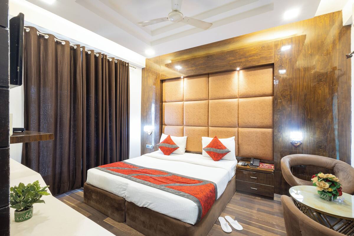 A hotel room with a large bed, a wooden headboard, a small table with a vase, and a chair.