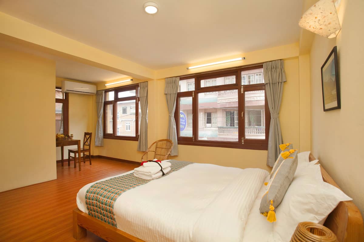 Una habitación de hotel con una cama grande, suelo de madera, un escritorio con silla y ventanas amplias con cortinas.