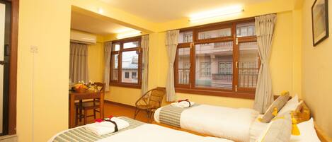 A hotel room with two beds, a wooden desk, a chair, and large windows with curtains.