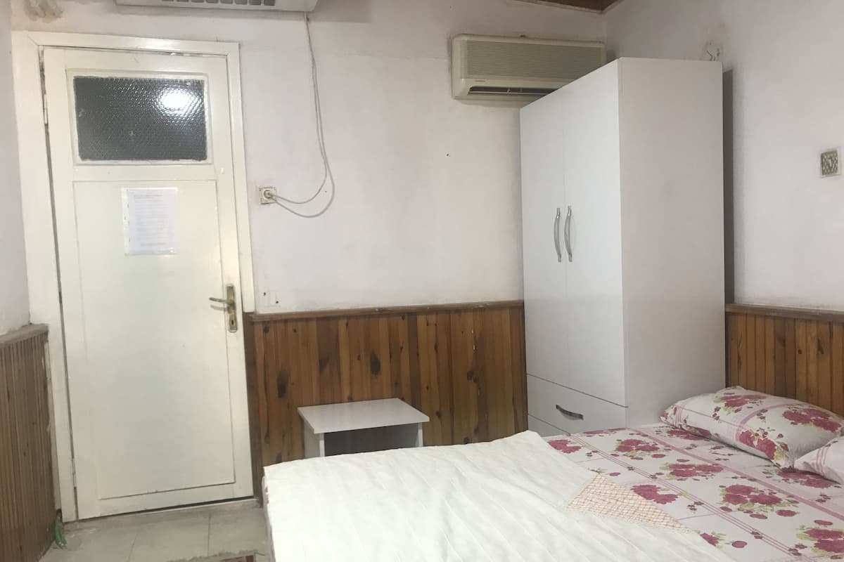 A bedroom with a bed, a wardrobe, a small table, and a door with a window.