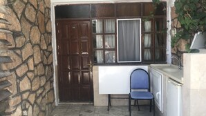 A small room with a stone wall, a wooden door, a window with curtains, a blue chair, and a white cabinet. - Kur-tur Otel (Denizli)