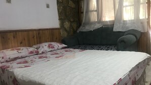 A bed with floral bedding, a stone wall, and a window with sheer curtains. - Kur-tur Otel (Denizli)