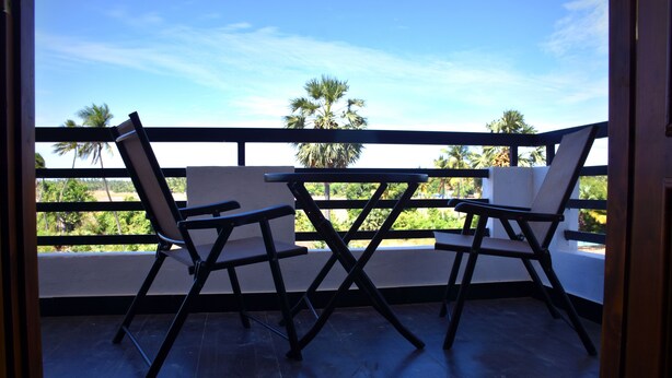 Varanda com duas cadeiras e uma mesa, com vista para uma palmeira e um céu limpo.