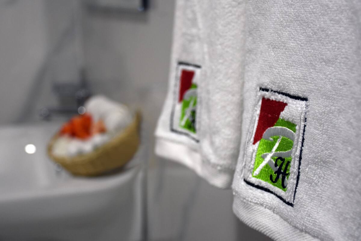 Ett badrum med en handdukshängare där en vit handduk och en mindre handduk med broderade logotyper hänger.