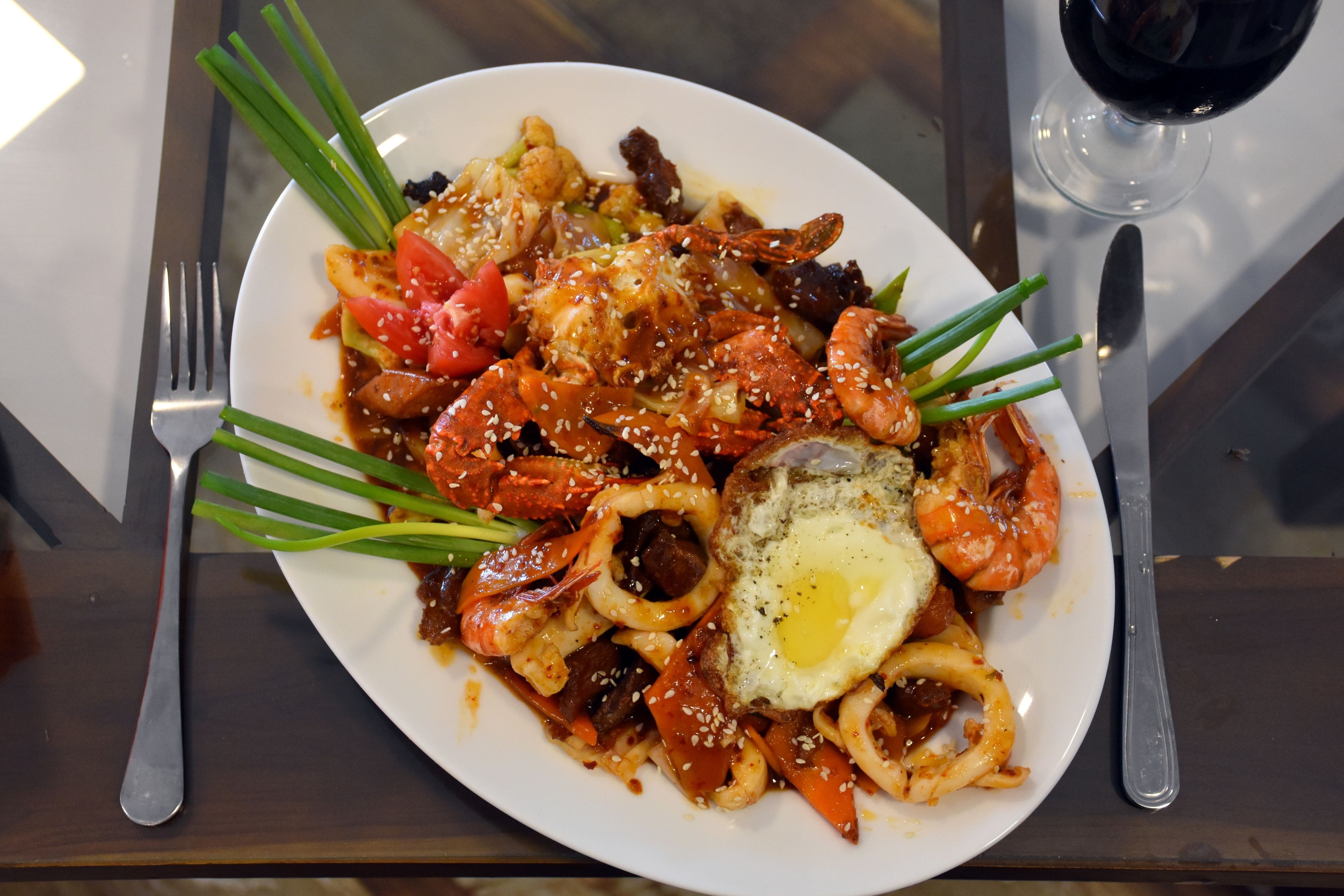Une assiette remplie de différents aliments, une fourchette, un couteau et un verre de vin rouge, le tout posé sur une table.
