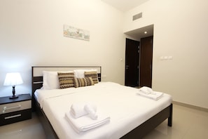 A neatly made bed with white linens and folded towels, a bedside lamp, and a wall-mounted artwork.