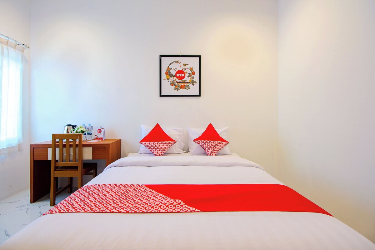Una habitació d'hotel amb un llit, una taula i una cadira. Hi ha un quadre al mur sobre el llit.