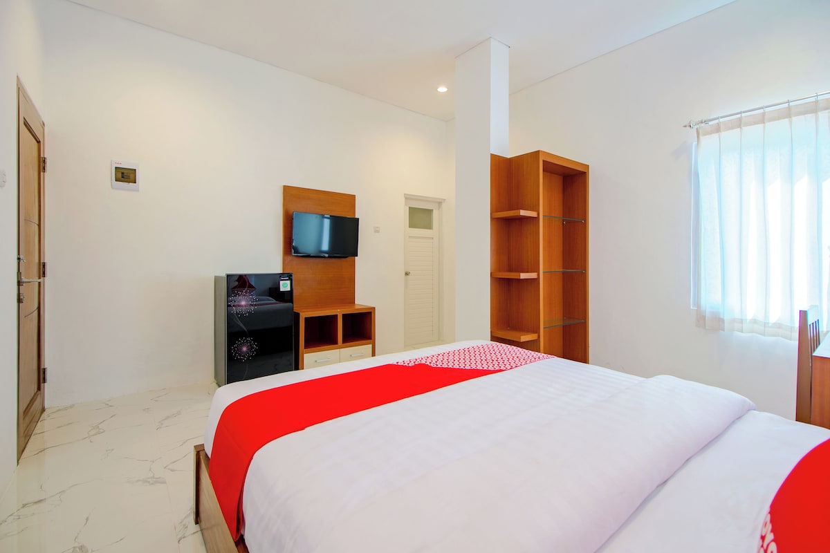 Habitación de hotel con cama, televisor, armario y ventana con cortinas.